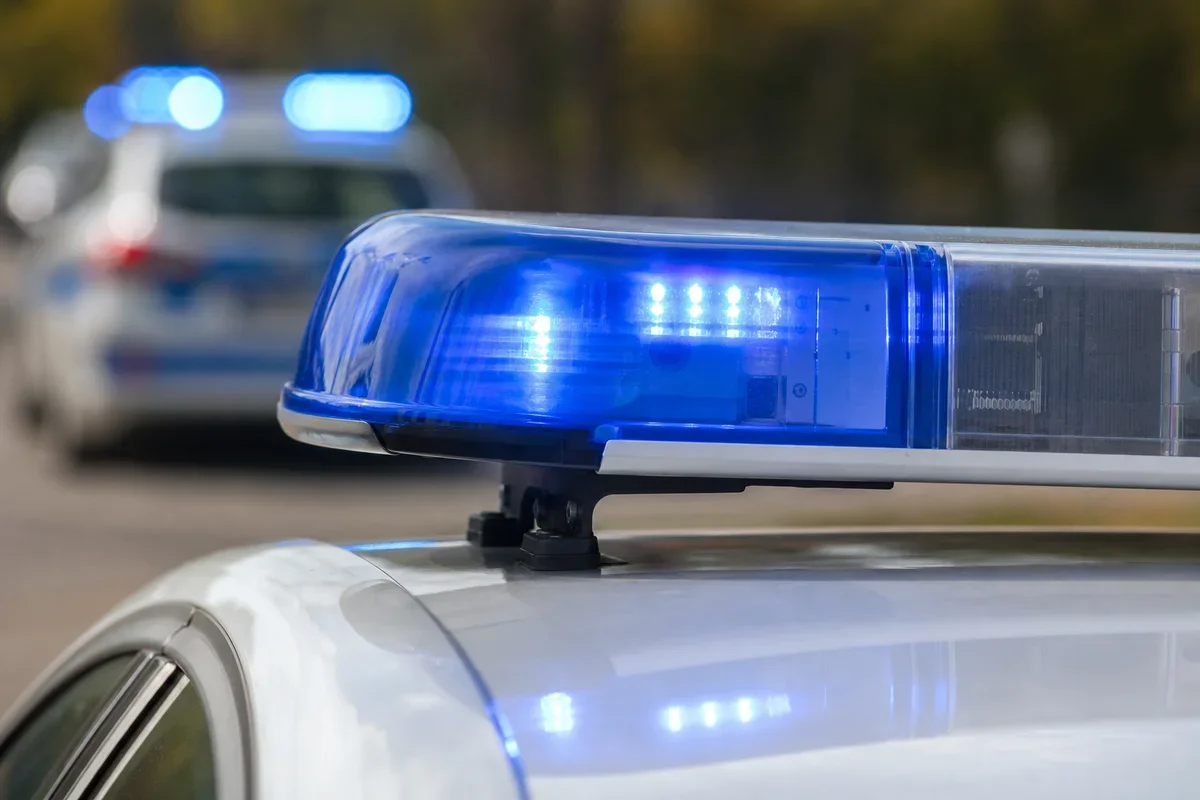 Zbliżenie na niebieskie światło policyjnego koguta na dachu radiowozu, w tle rozmyty drugi radiowóz z włączonymi błyskającymi światłami.