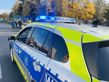Policyjny radiowóz z włączonym niebieskim światłem stoi na drodze w słoneczny, jesienny dzień.